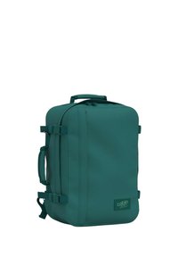 Zaino turchese di forma rettangolare, realizzato in tessuto resistente. Presenta una maniglia superiore, spallacci regolabili e una toppa con il logo sulla parte anteriore.