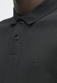 Dunkelgraues Polo-Shirt aus strukturiertem Stoff. Verfügt über eine Drei-Knopf-Leiste und ein dezentes gesticktes Logo auf der Brust.