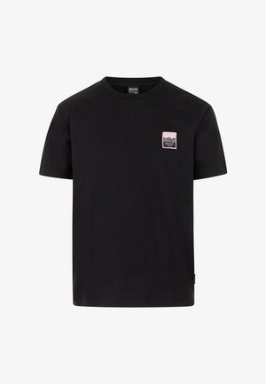 Camiseta negra de algodón con mangas cortas y cuello redondo. Destaca un pequeño parche de logo en rosa y verde en el área del pecho izquierdo.