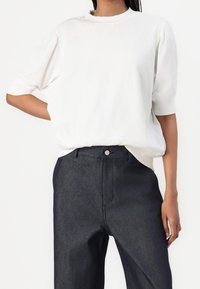 Vit kortärmad topp med rund halsringning, avslappnad passform och mjuk textur. Matchas med mörka denimhögmidjebyxor med en framficka.