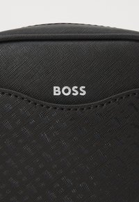 Borsa nera con texture, caratterizzata da una parte superiore liscia, una superficie con un motivo discreto e il logo "BOSS" in rilievo di colore bianco.