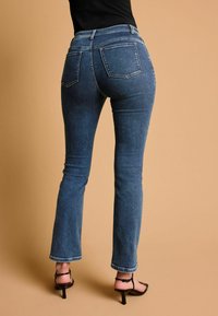Vaqueros azul oscuro de corte ajustado, con dos bolsillos traseros, un leve corte acampanado en el dobladillo y combinados con tacones negros de tiras.