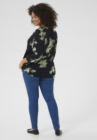Zwarte bloemenblouse met groen bloemenpatroon, lange mouwen en een comfortabele pasvorm. Gecombineerd met blauwe jeans en zwarte ballerina's.