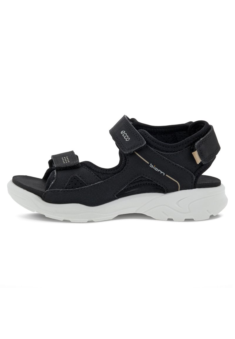 Svart sandal med en strukturerad design, utrustad med justerbara kardborreband och en kraftig vit sula. Tillverkad av andningsbara material med nätinslag.
