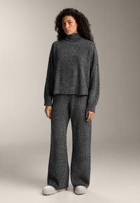 Sivý pletený sveter s vysokým golierom a dlhými rukávmi, spárovaný s nohavicami s širokými nohavicami v rovnakom odtieni. Materiál má textúrovaný vzhľad a voľný strih.