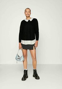 Sort langærmet sweater med en hvid krave, lagdelt over en lys grå bluse, parret med en sort miniskørt og sorte kampstøvler.