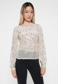 Blouse transparente à manches longues avec des sequins argentés verticaux sur une base rose pâle, présentant un ourlet froncé et des manches bouffantes.