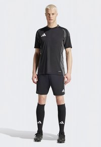 Μαύρη αθλητική στολή που περιλαμβάνει κοντομάνικο πουκάμισο, σορτς και κάλτσες μέχρι το γόνατο. Κατασκευασμένη από ελαφρύ ύφασμα με διαγώνια σχέδια και λογότυπα.