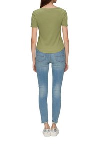 Olijfgroen korte mouwen top met een ronde zoom, gecombineerd met lichtblauwe skinny jeans en witte sneakers met een zilveren accent.