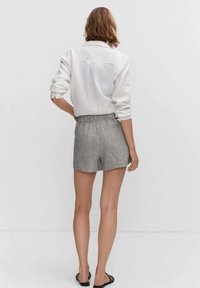 Valkoinen pitkähihainen paita, rento malli, yhdistetty harmaan ja valkoisen raidoitettujen shortstenn kanssa, joissa on joustava vyötärö. Mustat sandaalit täydentävät asua.