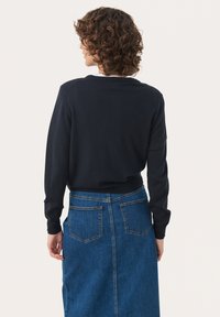 Dunkelblauer Pullover mit langen Ärmeln, leichtem Strick und gerippten Bündchen, kombiniert mit einem blauen Jeansrock mit hinteren Taschen und geradem Schnitt.