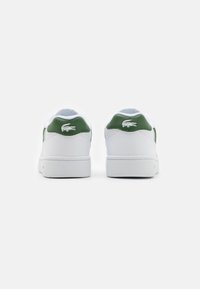 Zapatillas blancas con detalles en verde, material de piel suave, puntera redonda y suela de goma texturizada. Presenta un logo en el talón.