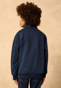 Navy sweatshirt with a high collar, loose fit, and ribbed cuffs. Soft texture with a solid color, back view displayed against a neutral background.