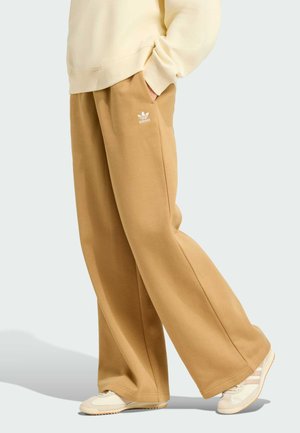 Beige sweatpants with a loose fit, made of soft fabric. Feature side pockets and a white adidas logo on the left thigh. Paired with light sneakers.