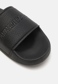 Sandalo con cinturino in pelle nera testurizzata con logo del marchio in rilievo. Plantare liscio e design della suola curva.