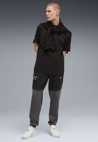 Zwarte t-shirt en grijze trainingsbroek met zwarte accenten. Witte sneakers. Trui om de schouders gedrapeerd. Minimalistisch sportief ontwerp.