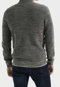 Harmaa neulottu korkeakauluksinen villapaita, jossa on tekstuurinen kuvio ja istuva malli. Päällä tummansinisten farkkujen kanssa.