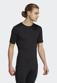 Svart T-shirt med kort ärm av ett mjukt tyg, figursydd design med rund hals och subtila sömdetaljer, bärs med svarta leggings.