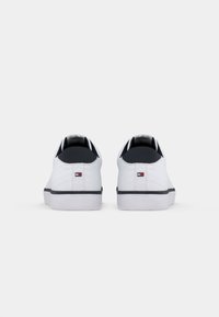 White sneakers with a smooth leather finish, black accents on the collar, and a white rubber sole. Includes subtle stitched detailing.