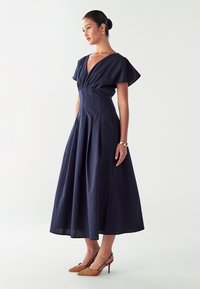 Tamnomodre obleka midi z kratkimi, rahlo zavihanim rokavi, prilegajočim se zgornjim delom in nabranim krilom. Nosite jo s svetlo rjavimi slingback petami z ostrim nosom.