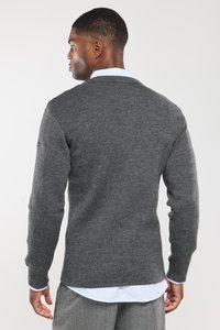 Pull en maille gris avec des manches longues, décolleté ras du cou, tissu texturé et côtes discrètes. Étiquette visible sur la manche gauche.