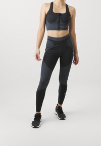 Completo di reggiseno sportivo e leggings in grigio scuro con pannelli neri a contrasto. Presenta una chiusura frontale con zip, una vestibilità strutturata e un materiale traspirante.