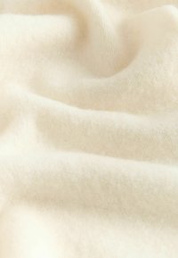 Pehmeä, kermaisen valkoinen kangas, jossa on sileä rakenne, hienovaraisia taitoksia ja herkkä, kevyt ilme, joka sopii täydellisesti vaatteisiin tai verhoiluun.