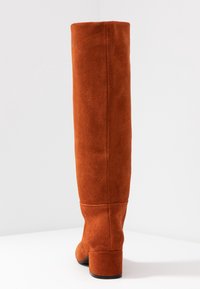 Botas altas de tacón en ante naranja. Textura suave, caña ajustada y tacón de bloque. Las costuras son visibles, lo que proporciona un diseño limpio.