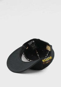 Musta baseball-lippalakki, jossa on kaareva lippareuna, varustettu brodeeratulla "Baker" -logolla ja sarjakuvakarhun grafiikalla sisällä. Sisäpuolella näkyy brändielementtejä.