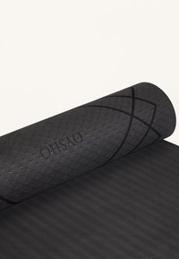 Svart yogamatta med texturerad yta som har cirkulära och vågmönster. Delvis rullad, visar en slät undersida med ränder.