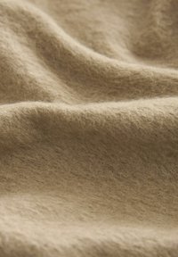 Tissu en laine beige doux avec des fibres visibles et des plis doux, mettant en valeur sa texture chaude et confortable.