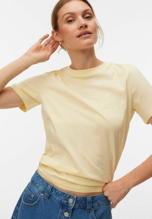 T-shirt di cotone giallo chiaro con maniche corte e collo rotondo, abbinata a jeans di denim blu a vita alta con dettagli a bottoni.