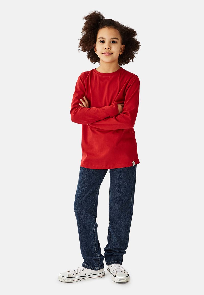 Langærmet rød bomuld T-shirt med rund hals, kombineret med mørkeblå jeans og hvide sneakers. Simpelt design uden mønstre eller detaljer.