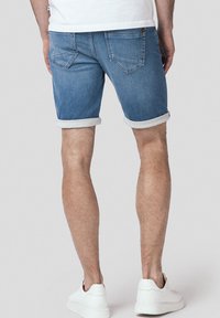 Jasnoniebieskie spodenki dżinsowe z podwiniętymi mankietami, dwoma tylnymi kieszeniami i detalem w postaci guzika. W zestawie z białymi sneakersami.