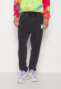 Schwarze, taillierte Jogginghose aus einem weichen, strukturierten Stoff. Mit elastischem Bündchen und Kordelzug, seitlichen Taschen und einem kleinen Logo-Patch.