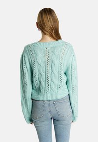 Maglione a trecce verde menta con vestibilità morbida, orlo a costine e dettagli a maglia aperta lungo la schiena e le maniche.