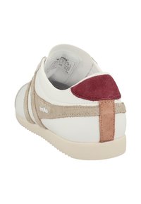 Sneaker bianca con accenti in suede beige e bordeaux, suola in gomma texturizzata e dettaglio del logo sul lato. La vista posteriore mostra materiali sovrapposti.