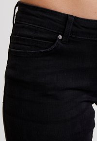 Jeans de mezclilla negra con una textura suave, con bolsillos frontales, una cinturilla clásica y un cierre de botón de metal.