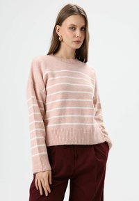 Roze gestreepte trui met een ronde hals, geribbelde zoom en brede mouwen, gecombineerd met donker bordeauxrode broek. Zachte textuur duidelijk zichtbaar.
