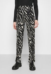 Svartvita zebra-mönstrade byxor med en figursydd midjeband, sidsprund vid fållen och ett texturerat tyg. Skor som visas är grova svarta kängor.