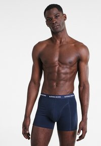 Boxer-culottes bleu marine en matériau doux, dotées d'une ceinture avec le logo blanc "BJÖRN BORG" et d'une coupe ajustée avec une poche à l'avant.