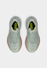 Ζευγάρι ανοιχτό πράσινα και ροδακινί αθλητικά παπούτσια με διάτρητο δίχτυ στο επάνω μέρος, λευκές σόλες και πέλματα "Neutral", φωτογραφημένα από πάνω σε λευκό φόντο.