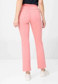 Rosa, dehnbare Stoffhose mit hohem elastischen Bund, zwei Gesäßtaschen und geradem Bein, kombiniert mit weißen Sneakers.