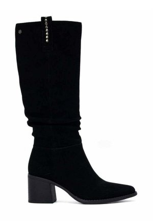 Bota negra de ante hasta la rodilla con tacón cuadrado y grueso y pequeños remaches decorativos plateados en la lengüeta de tirón cerca de la parte superior.
