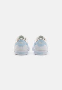 Baskets Nike blanches avec des accents bleu clair, un col rembourré et une tige en cuir lisse. Présente un logo en relief sur le talon et une semelle translucide.