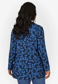 Blusa floreale con maniche lunghe, caratterizzata da uno sfondo nero e una stampa floreale blu, realizzata in tessuto leggero. Vista posteriore mostrata.
