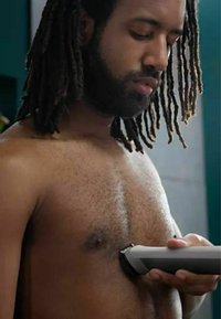 Body hair trimmer with a grey and black design, used on a bare chest. Close-up view highlighting trimming action and skin texture.