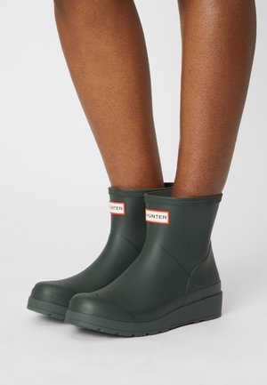 Botas de tobillo de goma verdes con un acabado mate, que presentan un logo en rojo y blanco, puntera redonda y suela texturizada para mayor agarre.