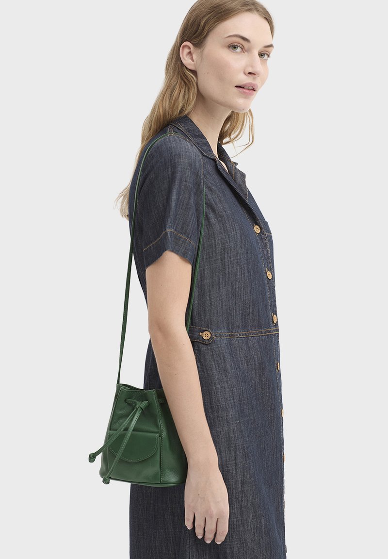 Robe-chemise en denim bleu avec manches courtes et fermeture à boutons, associée à un petit sac seau en cuir vert avec fermeture à cordon.