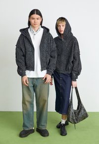 Black zippered hoodies with textured patterns, paired with light blue jeans and a dark blue denim skirt. Accessories include a patterned bag and footwear.
